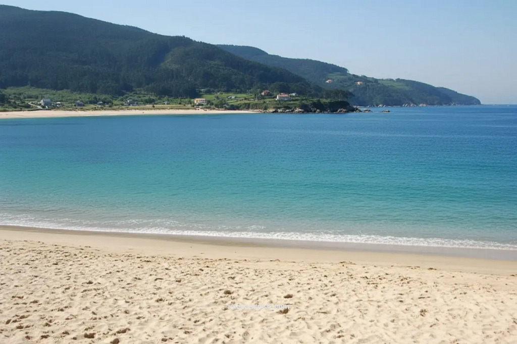 Wide turquoise bay and long sandy beach in Celeiro on the northern Spain coastline with green hills behind.