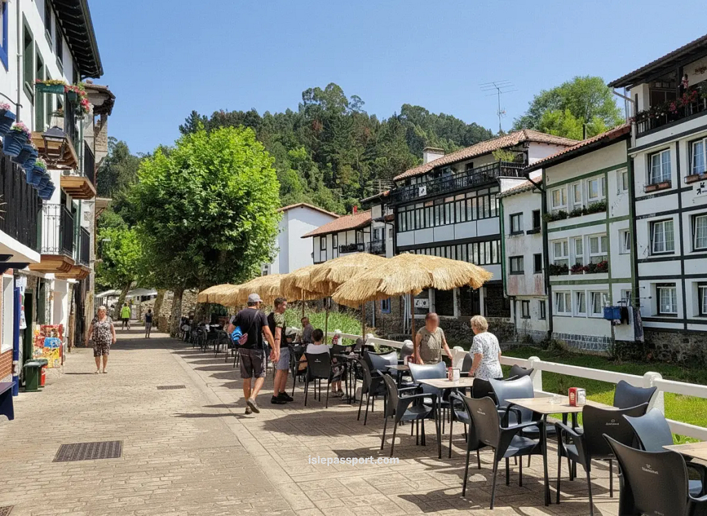 Riverside street in Ea, Basque Country, on the northern Spain coastline with Basque houses, café terraces, and forested hills.