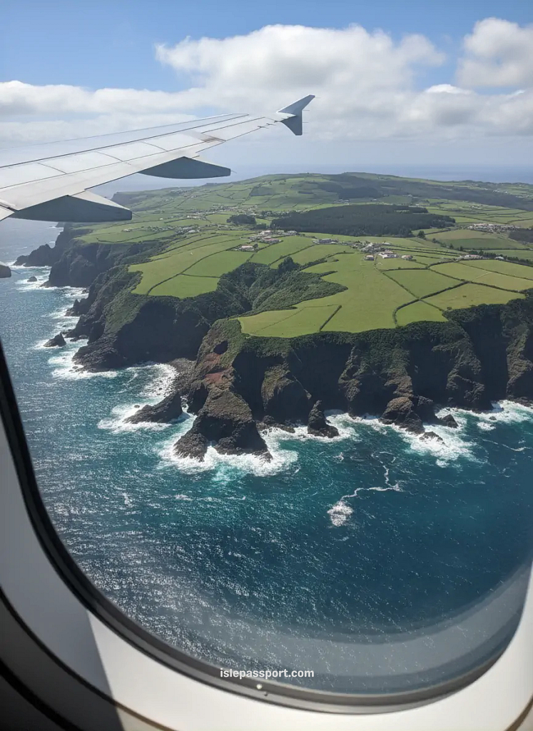 Aerial view of a volcanic island coastline from airplane window with cliffs, meadows, and waves breaking along rugged shores
