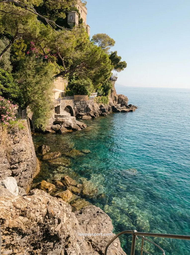 The rocky coastline of Santa Margherita Ligure featuring crystal clear turquoise water and lush green pine trees along the cliffs.