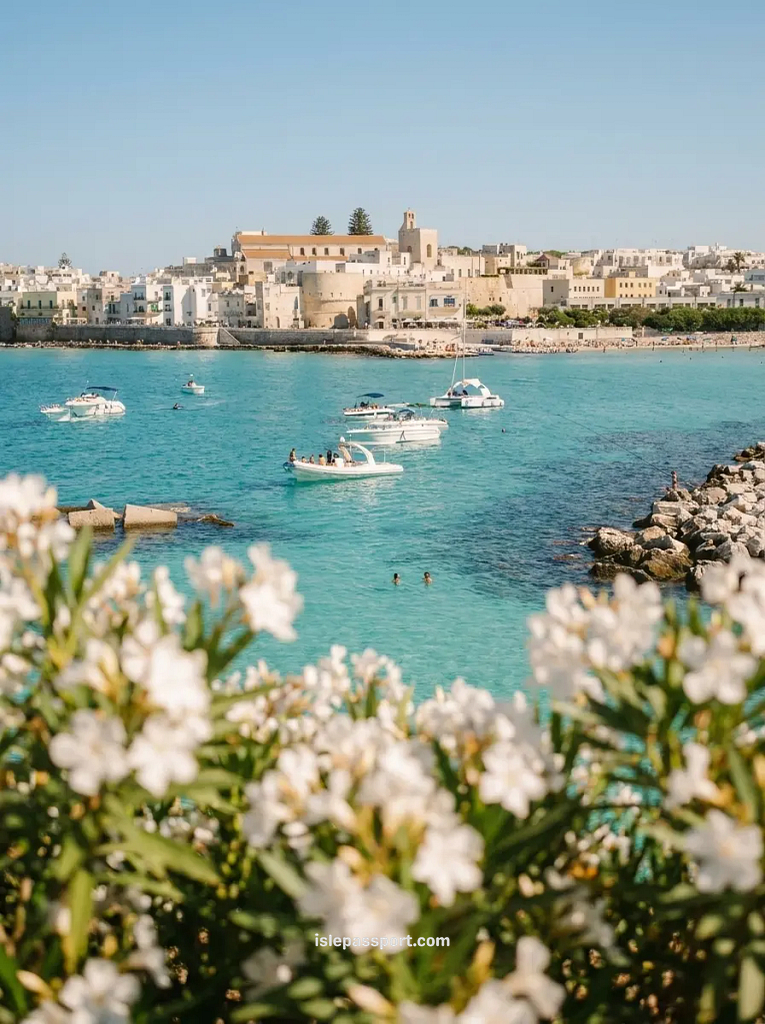 Otranto harbour and Aragonese castle walls seen across turquoise water with white oleander flowers in the foreground in Puglia