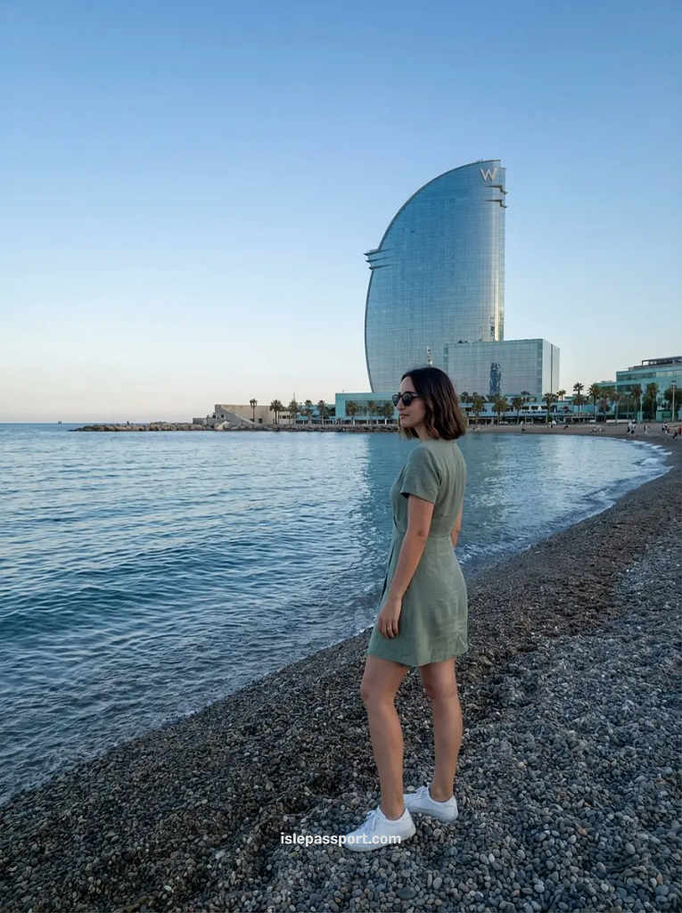 A woman standing on the pebble shore of Barceloneta beach in Barcelona with the sail-shaped W Hotel in the distance.