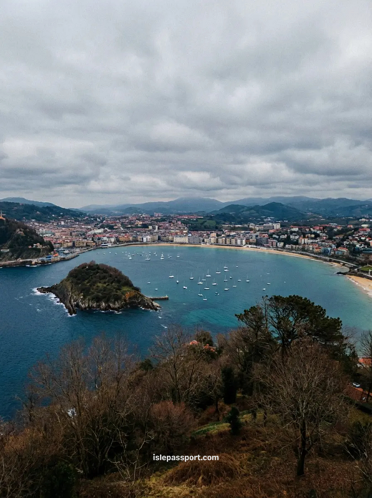 A view of the dramatic La Concha bay in San Sebastián during winter, with moody skies over turquoise water, showcasing alternative options for Spanish coastal living.