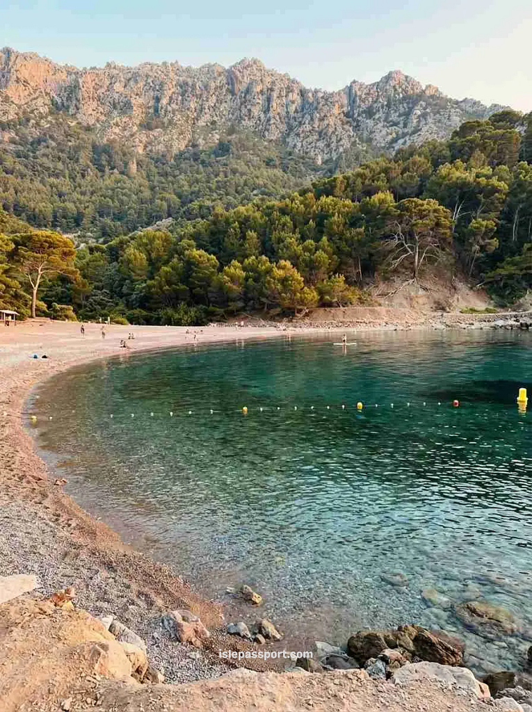 Landscape view of the pebble shore and green water of Cala Tuent set beneath the Serra de Tramuntana mountains, a unique Mallorca hidden beaches location.