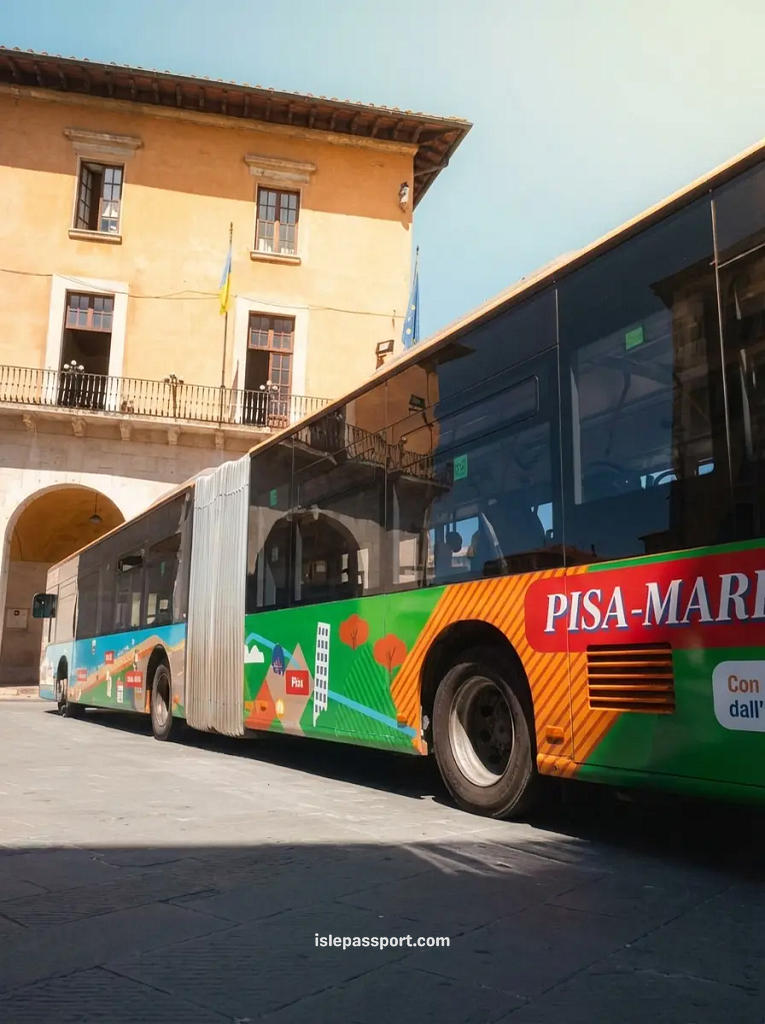 A colorful 'Pisa-Marina' bus parked in a sunlit Italian piazza in front of a historic orange building.
