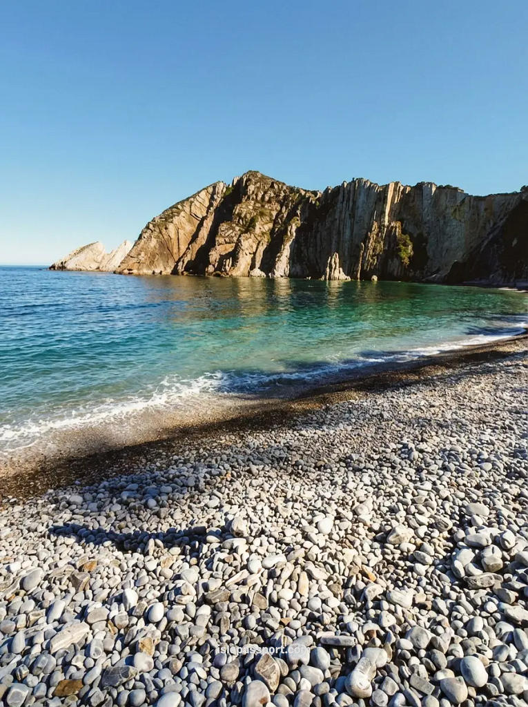 A wide view of the crescent-shaped Playa del Silencio in Asturias, showing a pebble beach enclosed by massive, vertical rock cliffs and emerald green Atlantic water.