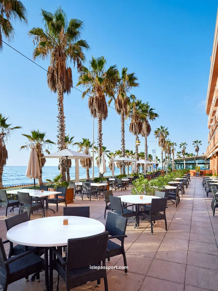 A sunny outdoor terrace at Restaurant Vento in Sitges with white umbrellas and a view of the Mediterranean Sea.