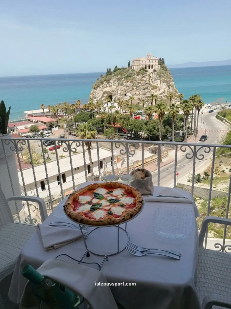 A delicious margherita pizza on a balcony overlooking the Sanctuary of Santa Maria dell'Isola in Tropea, Calabria.