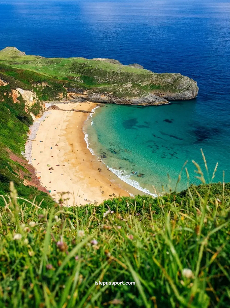 A high-angle view of a secluded turquoise cove in Asturias, Northern Spain, surrounded by dramatic lush green cliffs and rugged rock formations.