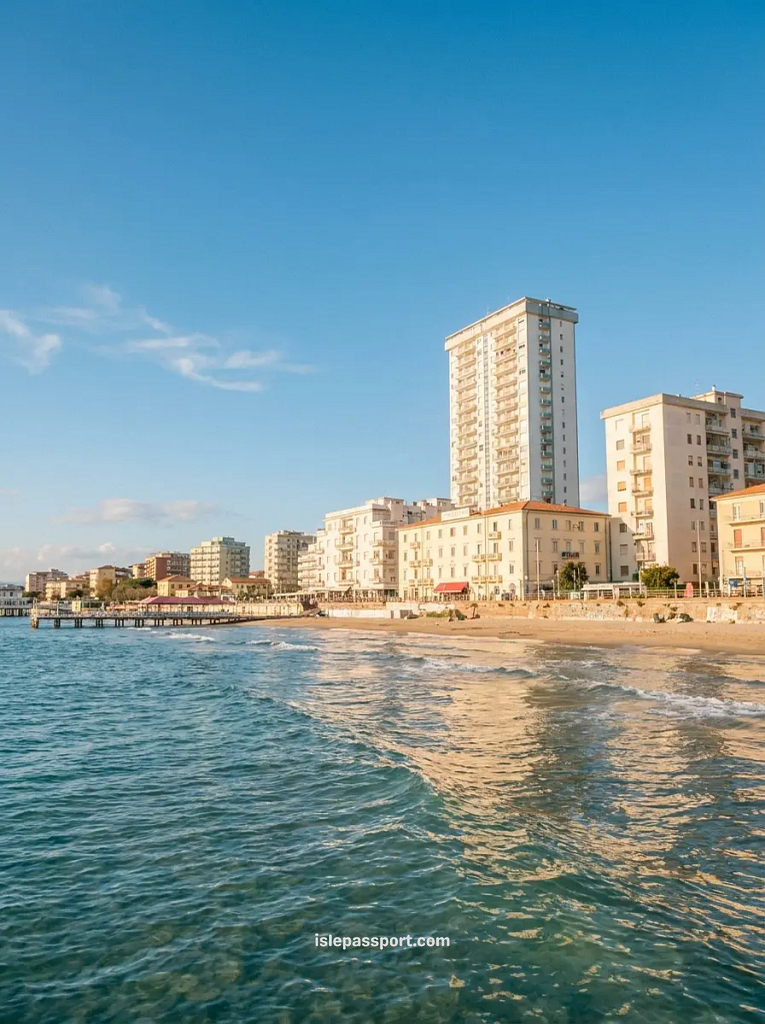 Looking down the sandy shoreline of Follonica, showing the calm waves of the sea reflecting the tall waterfront hotels and apartment blocks during a clear afternoon trip.