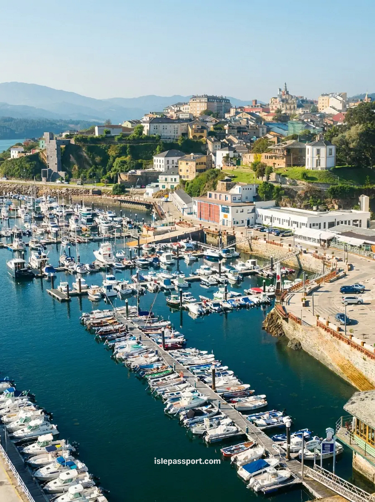 Aerial view of Ribadeo's busy marina packed with white boats, with the historic hilltop town and green mountains rising behind it on the Galician coast of northern Spain