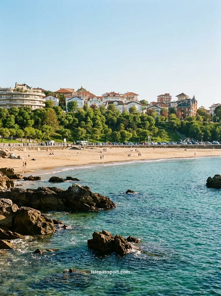 Turquoise water lapping over coastal rocks in front of a sandy beach in Santander, with green hillside and elegant villas visible behind the shoreline in northern Spain