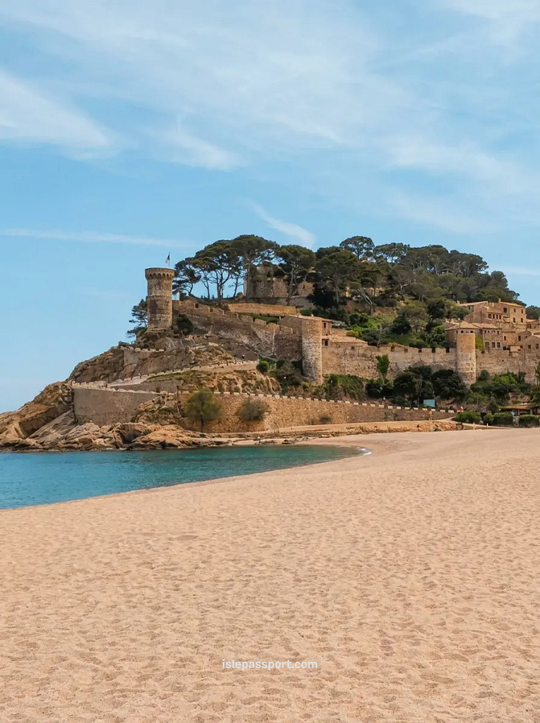 The wide golden sand beach of Tossa de Mar in Costa Brava with the ancient medieval walled fortress on the hill overlooking the sea.