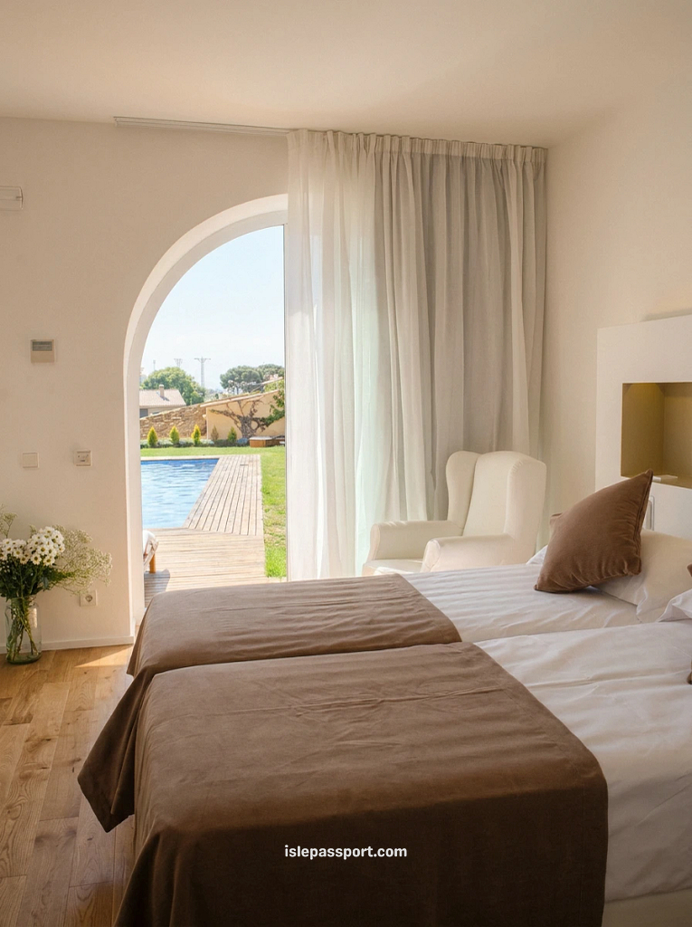 White hotel bedroom with an arched glass doorway opening directly to a sunny outdoor swimming pool at Hostalet de Begur.