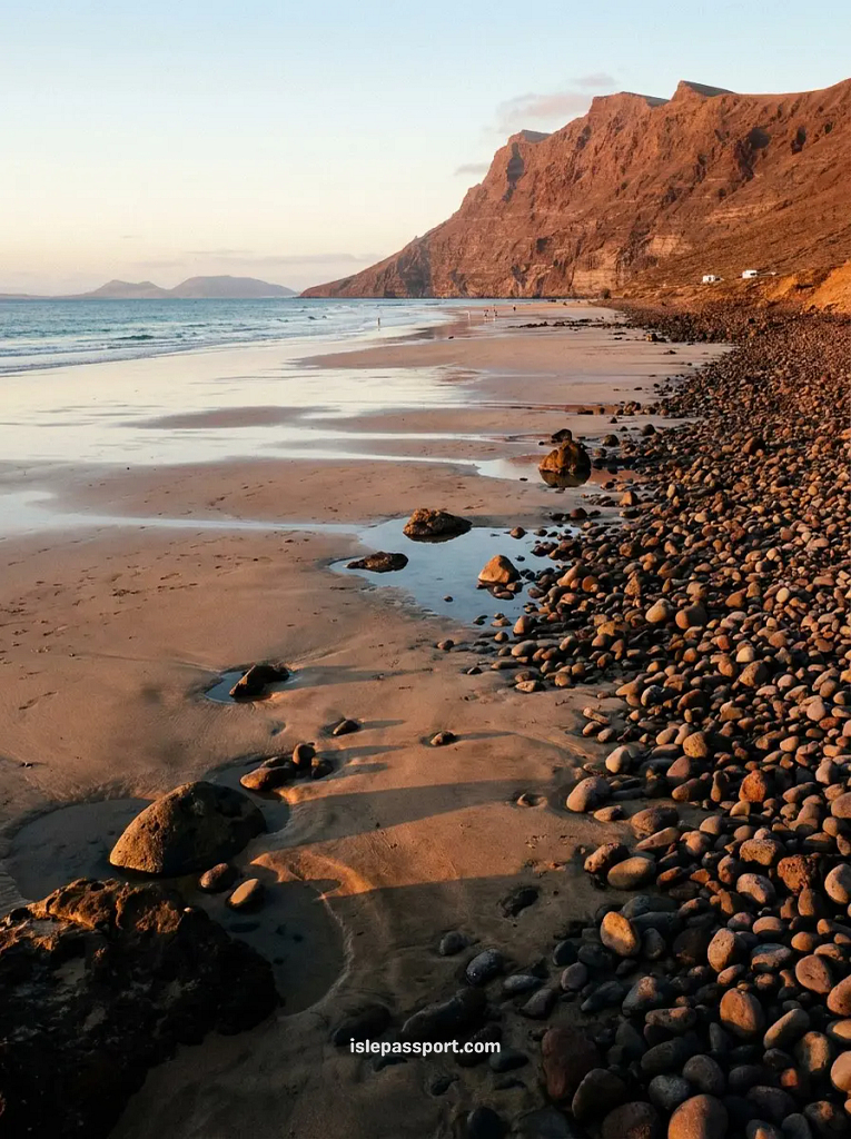 Famara beach in Lanzarote in winter at low tide, pebbles and wet sand under warm dusk light