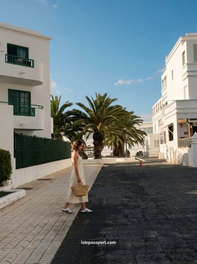 Maya walking past white apartment buildings and palm trees on a quiet street in Costa Teguise, Lanzarote