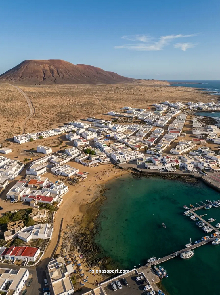 Aerial view of Caleta de Sebo on La Graciosa, with white houses, sandy streets, the harbour and a volcano behind