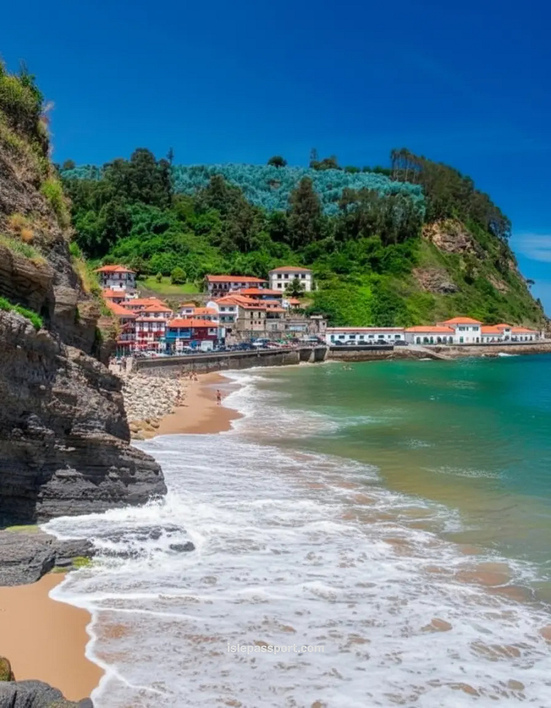 Cliffside view of Tazones on the underrated northern Spain coast with colorful houses, a small beach, and green hills.